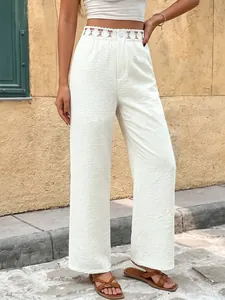 Dettaglio dei pantaloni bianchi a gamba larga con vita traforata in pizzo chic
