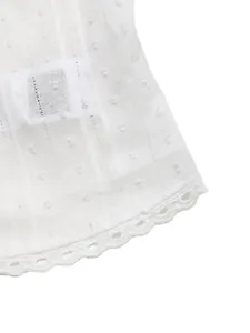 Close-up van de witte jacquard stof en de kanten rand van een mouwloze V-hals topje.