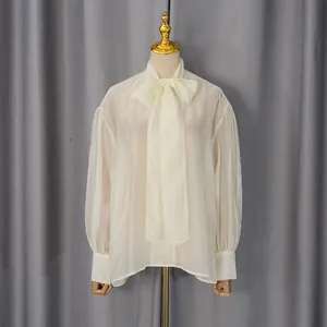 Detalle de blusa blanca de gasa con lazo en cuello y mangas abullonadas transparentes.