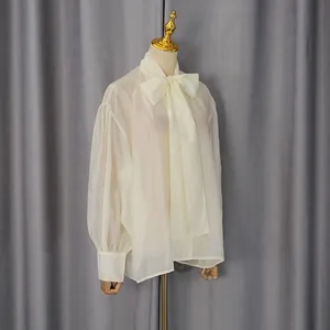 Elegante blusa de gasa beige transparente con lazo grande en un maniquí