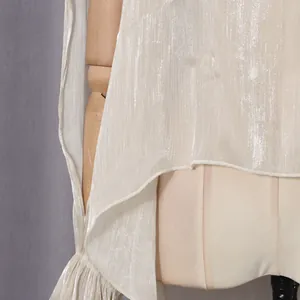 Detailaufnahme einer schimmernden weißen Langarmbluse mit drapiertem Saum und Rüschen