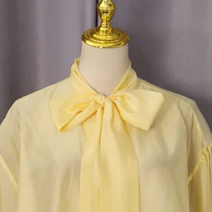 Primer plano detallado de una elegante blusa amarilla con lazo en tela ligera y transpirable
