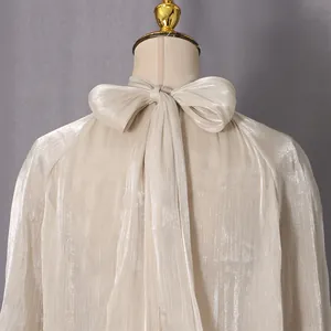 Detailansicht einer elegant schimmernden schulterfreien Langarmbluse mit Schleife hinten.