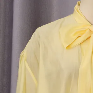 Vista de detalle de una blusa amarilla con lazo en el cuello y tejido de textura suave