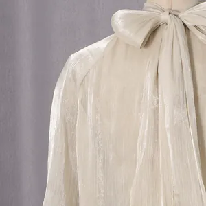 Detail einer schimmernden champagnerfarbenen Bluse mit einer eleganten Schluppen-Schleife.
