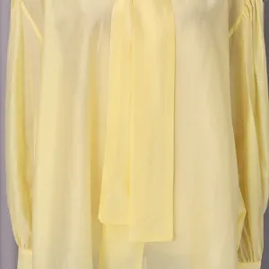 Detalle de una blusa de verano amarillo pálido con elegante cuello lazo y tejido con textura.
