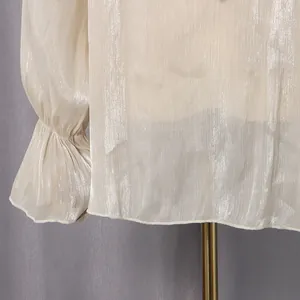 Detailansicht des schimmernden champagnerfarbenen Crinkle-Stoffs an einer eleganten Bluse
