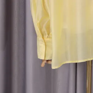 Primer plano del puño y los botones de una blusa ligera de color amarillo suave.