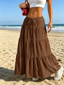 Dettaglio di una gonna lunga marrone a balze con coulisse in vita su una spiaggia.