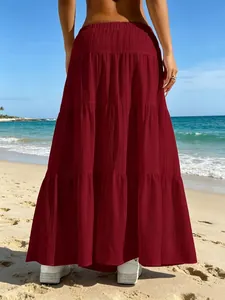 Elegante gonna lunga a balze bordeaux da donna mostrata su una spiaggia soleggiata da dietro