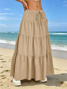 Dettaglio di una gonna maxi beige a balze con coulisse in vita e tessuto plissettato in spiaggia