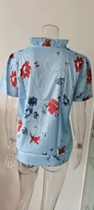 Vista posteriore della camicetta azzurra da donna con fiori e colletto a volant.