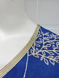 Detailed view of gold braided trim and exquisite leaf embroidery on blue fabric dress
