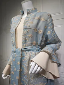 Dettaglio dell'elegante cardigan blu con ricami floreali e maniche a campana su abito beige