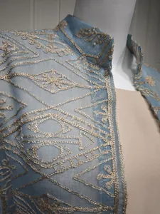 Primo piano dettagliato del ricamo dorato su un elegante cardigan in tessuto blu velato