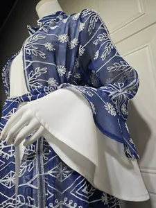 Dettaglio dell'elegante cardigan blu ricamato con ampie maniche a campana bianche a strati.