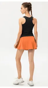 Mujer con top deportivo negro y falda de tenis naranja para entrenamiento fitness