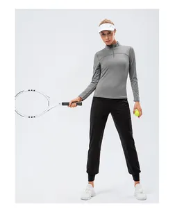 Female athlete in grey half-zip sports top and black joggers holding a tennis racket