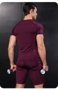 Achteraanzicht van een man in een bordeauxrode compressie fitnessset met zware dumbbells.