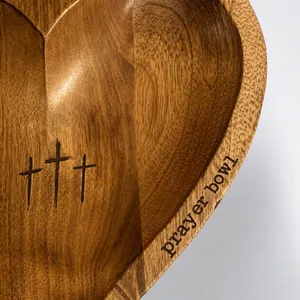 Macro detail of hand-carved heart-shaped wooden prayer bowl with cross engraving