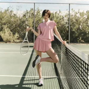 Female athlete in a pink contrast polo tennis suit and pleated skirt on a court.