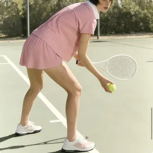 Female athlete in pink tennis outfit with pleated skirt on green court action shot