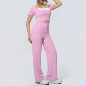 Full-body studio shot of a woman wearing a pink two-piece yoga set with wide-leg pants