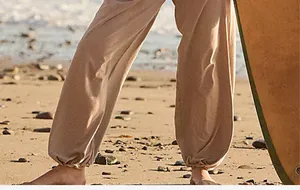 Close-up of tan jogger pants with elastic cuffs on a sandy beach background