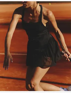 Professional action shot of a black mesh panel tennis dress on a red clay court