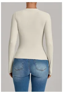 Detailed back view of a slim-fit cream long-sleeved athletic yoga top worn with denim jeans.