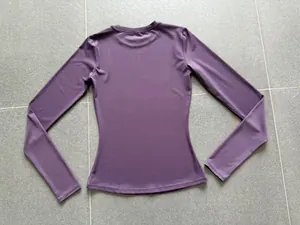 Back view of a purple long-sleeved yoga top with a tight, form-fitting design on tiles.