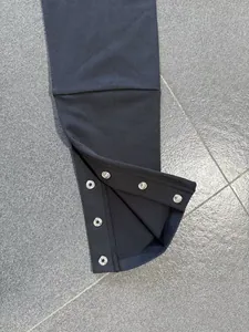 Detailansicht der verstellbaren Druckknopfschlitze am Saum schwarzer Yoga-Schlaghosen.