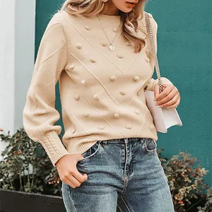 Detailed close-up of beige knit sweater featuring pom-pom accents and elegant chevron patterns