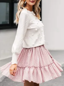 Detail shot of elegant white crew neck knit sweater featuring pom-pom decorations