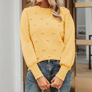 Detailed view of yellow long-sleeve knit sweater featuring decorative pom-poms and textured V-pattern