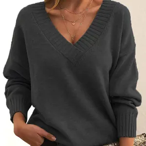 Close-up detail of a dark grey loose-fit V-neck knit pullover with ribbed textures and gold accessories