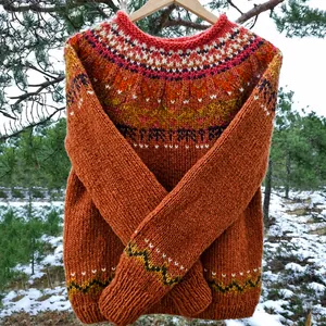 Dettaglio di un maglione rustico in maglia Fair Isle appeso in una foresta innevata