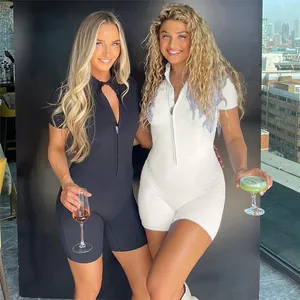 Two models wearing black and white tight short-sleeve yoga jumpsuits with zip front detail
