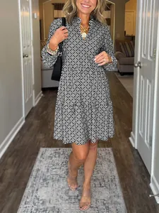 Caucasian model wearing a V-neck geometric print tiered dress with three-quarter sleeves.