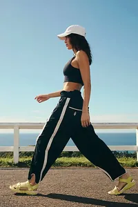 Hoch taillierte schwarze weite Freizeithose mit Seitenstreifen auf einem Küstenweg