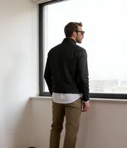 Rear view of a minimalist black stand-collar jacket for men in a bright indoor setting