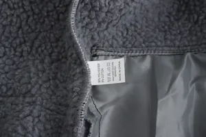 Detailopname van de grijze fleece stof en het witte wasvoorschrift label van de jas
