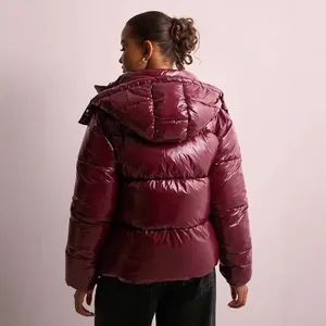 Back view detail of a woman wearing a shiny burgundy hooded puffer jacket for winter season