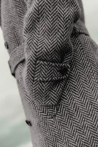 Gros plan détaillé de la manche d'un manteau en laine à chevrons avec détail de bouton