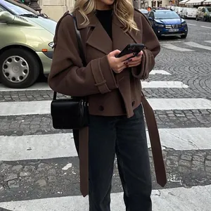 Veste chic en laine marron avec une taille ceinturée dans un décor urbain de rue.