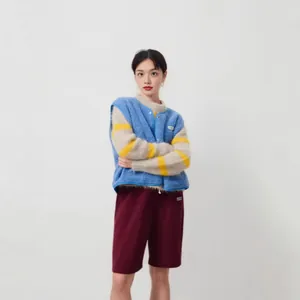 Femme en gilet polaire bleu sur un pull duveteux à rayures et un short bordeaux, style décontracté.