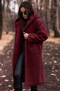 Woman wearing a burgundy long hooded teddy coat in a scenic autumn forest park setting.