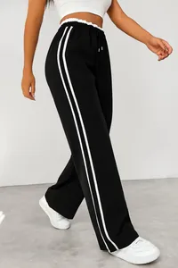 Detail of black wide-leg sweatpants with white side stripes worn by a model walking