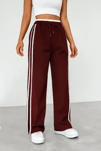 Detail showing the high waist and side stripe design of burgundy wide-leg sports pants.