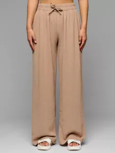 Detail view of high-waisted beige wide-leg trousers with textured fabric and drawstring.